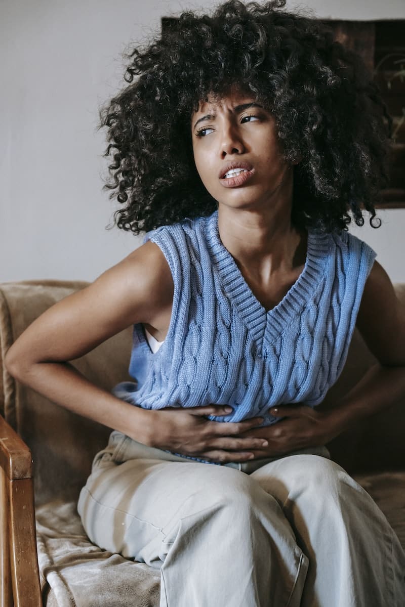 Young African American female sitting on couch at home while having acute pain in stomach